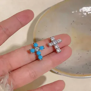 Primo piano di orecchini a lobo a forma di croce con pietre blu e zirconi chiari