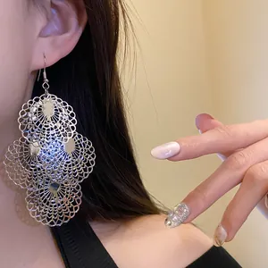 Detailed view of large silver metal hollow lace cutout dangle earrings worn by a model