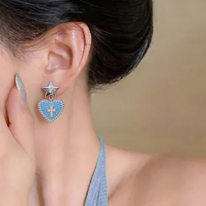 Vista dettagliata di un elegante orecchino a cuore blu con croce indossato sull'orecchio