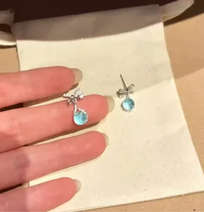 Detailed view of elegant bow-shaped silver earrings with sea blue zircon drop pendants