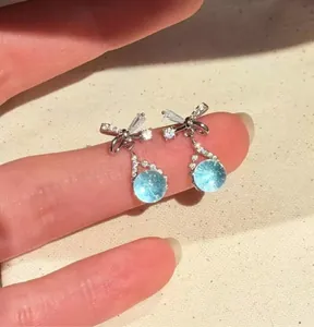 Detail view of elegant blue water drop zircon earrings with bow design on fingers