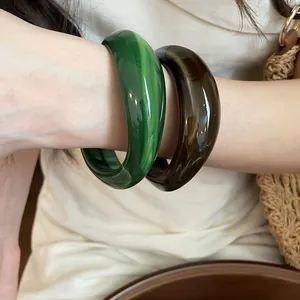 Close-up of irregular geometric acrylic marbled bangles in green and amber brown.