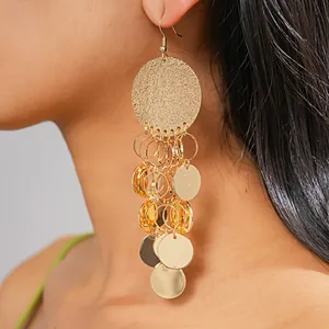 Close-up view of gold metallic disc sequin tassel drop earrings on model's ear