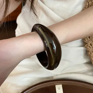 Close-up of a dark marbled acrylic bangle with irregular geometric design on a model's arm.