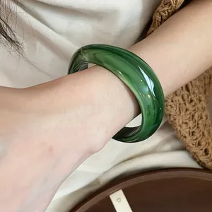 Macro view of an irregular green marbled acrylic bangle on a person wrist for fashion
