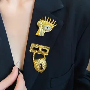 Close-up of vintage style gold lock and surrealist eye brooches on a black blazer