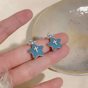 Primo piano di orecchini a stella con zirconi blu e un elegante design a croce