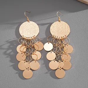 Close-up of oversized gold-tone chandelier earrings with tiered metallic round sequins.