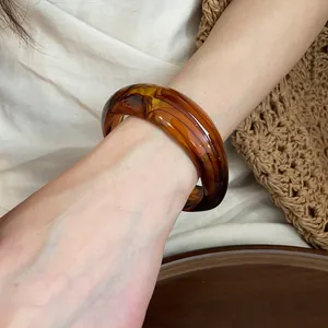 Detail view of stylish amber marbled acrylic bangle worn on wrist for minimalist look