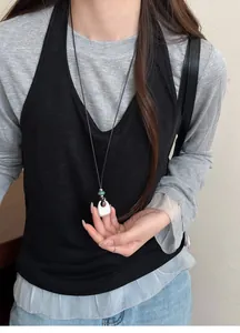 A detailed close-up shot of a minimalist silver water drop pendant necklace on a black vest