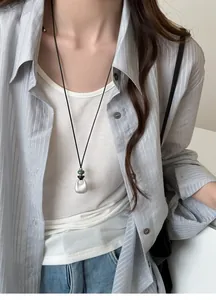 Detail of minimalist silver teardrop pendant on a long black cord worn with a shirt