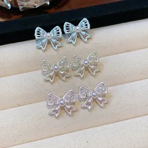 Detail view of silver needle hollow bow earrings with elegant central pearl accents
