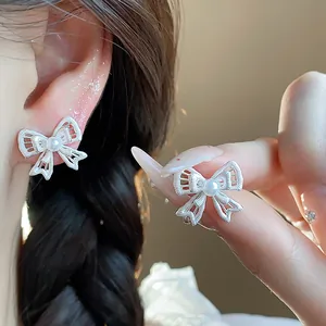 Detailed view of hollow bow stud earrings with a central pearl worn by an Asian model