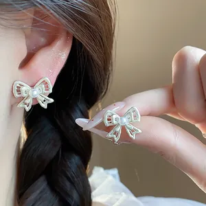 Close-up of elegant hollow bow pearl earrings displayed on ear and held by hand