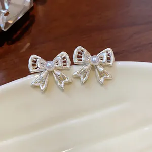Macro view of delicate hollowed bow-knot earrings with small central pearl detail