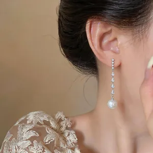 Close-up detail of silver zircon drop earrings with a round pearl pendant on a model