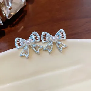 Macro view of delicate silver hollow-out bow stud earrings featuring a central white pearl