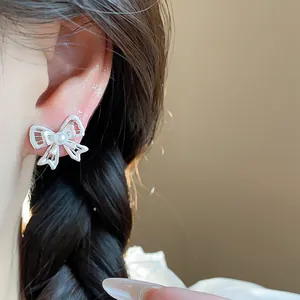 Close-up detail of hollow silver bow stud earrings featuring a center pearl accent