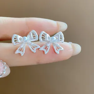 Close-up of elegant silver hollow bow-knot stud earrings with central pearl detail