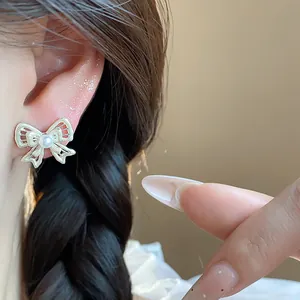 Detail view of exquisite hollow bow stud earrings with pearls worn on an elegant model