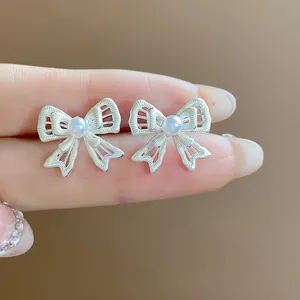 Close-up of elegant hollow silver bow stud earrings with a central pearl detail.
