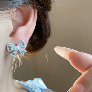 Detailed close-up view of a delicate hollow silver bow earring with a pearl on model ear