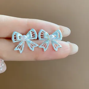 Close-up view of silver-plated openwork bow stud earrings featuring a central white pearl.