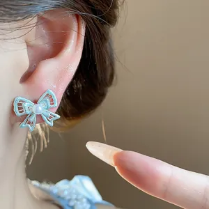 Close-up detail of silver hollow bow-knot stud earring with central pearl.