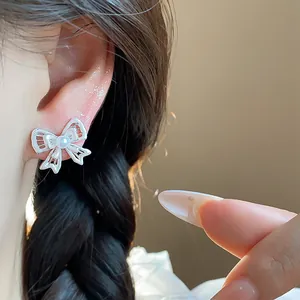 Close-up detail of exquisite silver needle hollow bow stud earrings with a pearl