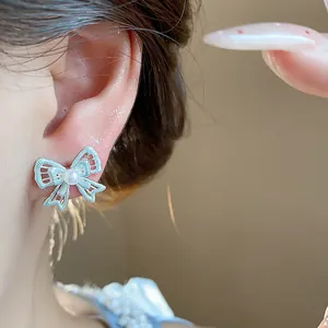Detailed view of elegant hollow silver bow stud earrings with a central pearl on the ear.