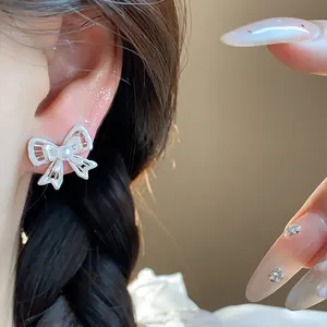 Detail view showing a hollow bowknot stud earring with a central pearl on the ear
