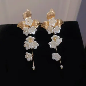 Detail of elegant floral drop earrings with white petals and gold leaf accents on black.