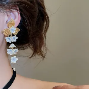 Detailed view of elegant white flower tassel earrings with gold leaf accents on a model