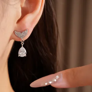 Detail of silver fish tail earrings with teardrop zircon worn on ear
