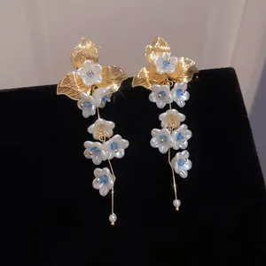 Macro detail of French flower tassel earrings with gold leaves, white petals and pearls