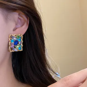 Dettaglio di orecchini vintage a bottone quadrati con strass colorati sull'orecchio del modello