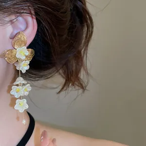 Close-up of French style golden floral tassel earrings with delicate white flowers and pearl