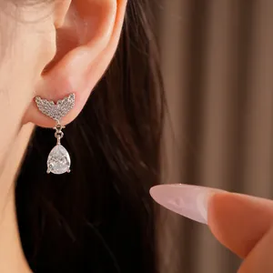 Macro view of elegant fish tail stud earrings with sparkling teardrop zircon on model ear