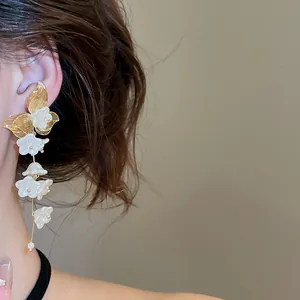 Close-up of elegant gold leaf and white flower tassel earrings worn on ear.