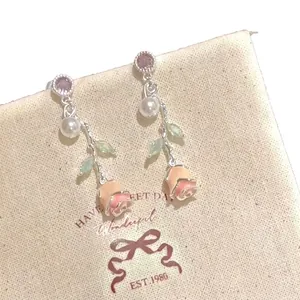 Elegant silver rose drop earrings with pearls and purple zircons displayed on a canvas pouch