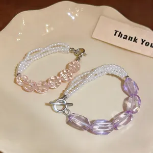 Dettaglio di bracciali a più fili con perle e cristalli sfaccettati su un piatto crema