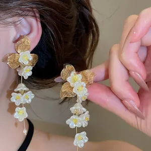 Detail of French floral tassel earrings with white petals and gold leaf accents.