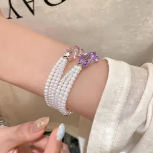 Primo piano di un elegante bracciale di perle multistrato con ciondoli in cristallo viola e rosa.