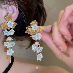 Macro view of French style floral tassel earrings with white pearls and gold metal leaves