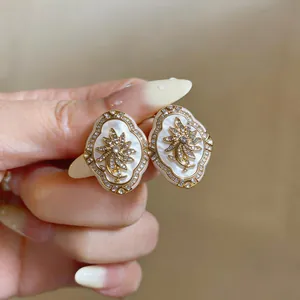 Close-up of elegant gold flower stud earrings with mother-of-pearl and crystal details