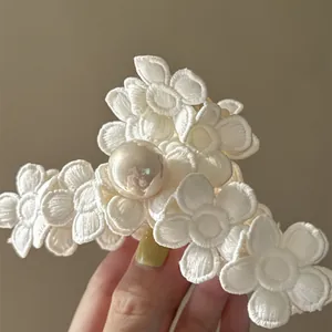 Gros plan sur une pince à cheveux française avec des fleurs brodées blanches et une perle