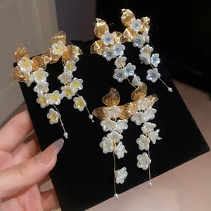 Close-up view of elegant white flower tassel earrings with gold leaves on black velvet.