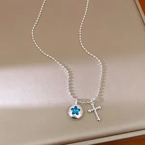 Silver beaded necklace with blue star pendant and cross charm on a beige background