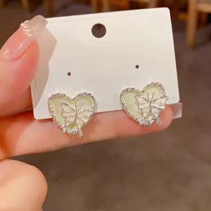 Détail de clous d'oreilles papillon en argent sur base en émail vert en forme de cœur.