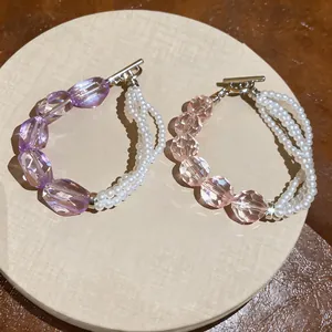 Primo piano di bracciali di perle multistrato con perle sfaccettate viola e rosa e chiusura OT.